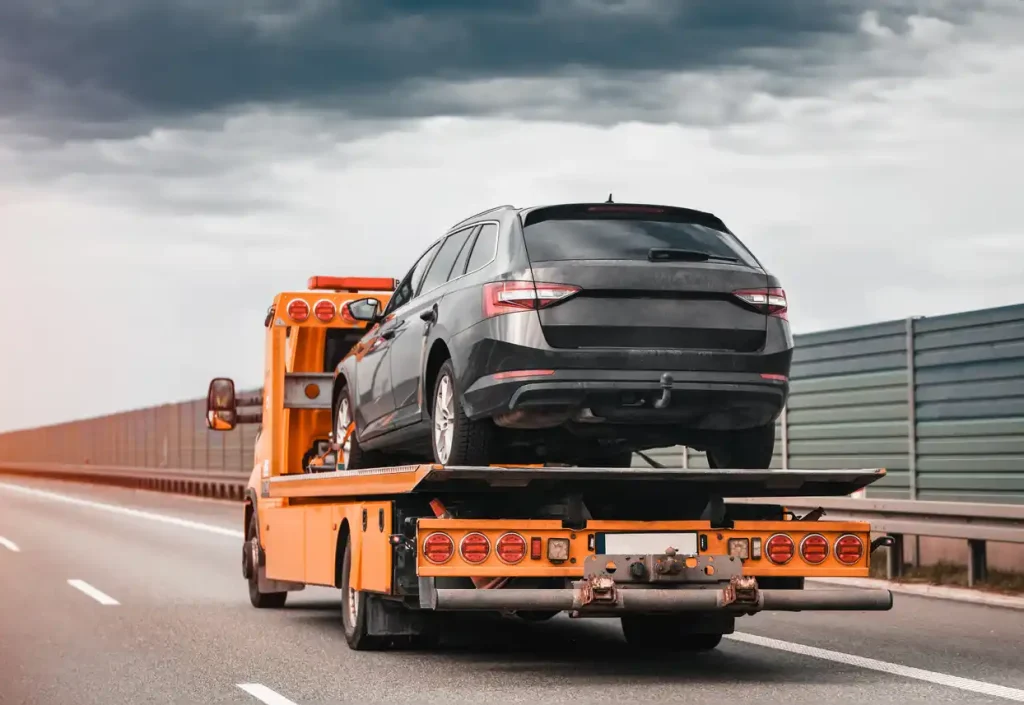 Oranger Abschleppwagen transportiert dunklen Kombi auf der Autobahn. Autoguru24/7 bietet deutschlandweite, kostenlose Abholung für Autos mit Schaden.