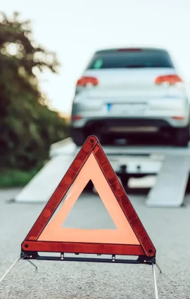Aufgestelltes Warndreieck vor einem Auto auf dem Abschleppwagen am Straßenrand. Autoguru24/7 holt Fahrzeuge mit Panne oder Schaden sicher und fachgerecht ab.